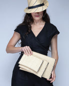Model wearing Amelia Set of 3 Natural straw color Nesting Zippered Straw Clutches Solid Colors handmade loomed raffia in a solid hue with matching zipper and braided zipper pull with cross stitch edging in three sizes of small, medium, and large - Shebobo (with Fedra Fedora Unisex Straw Sun Hat)