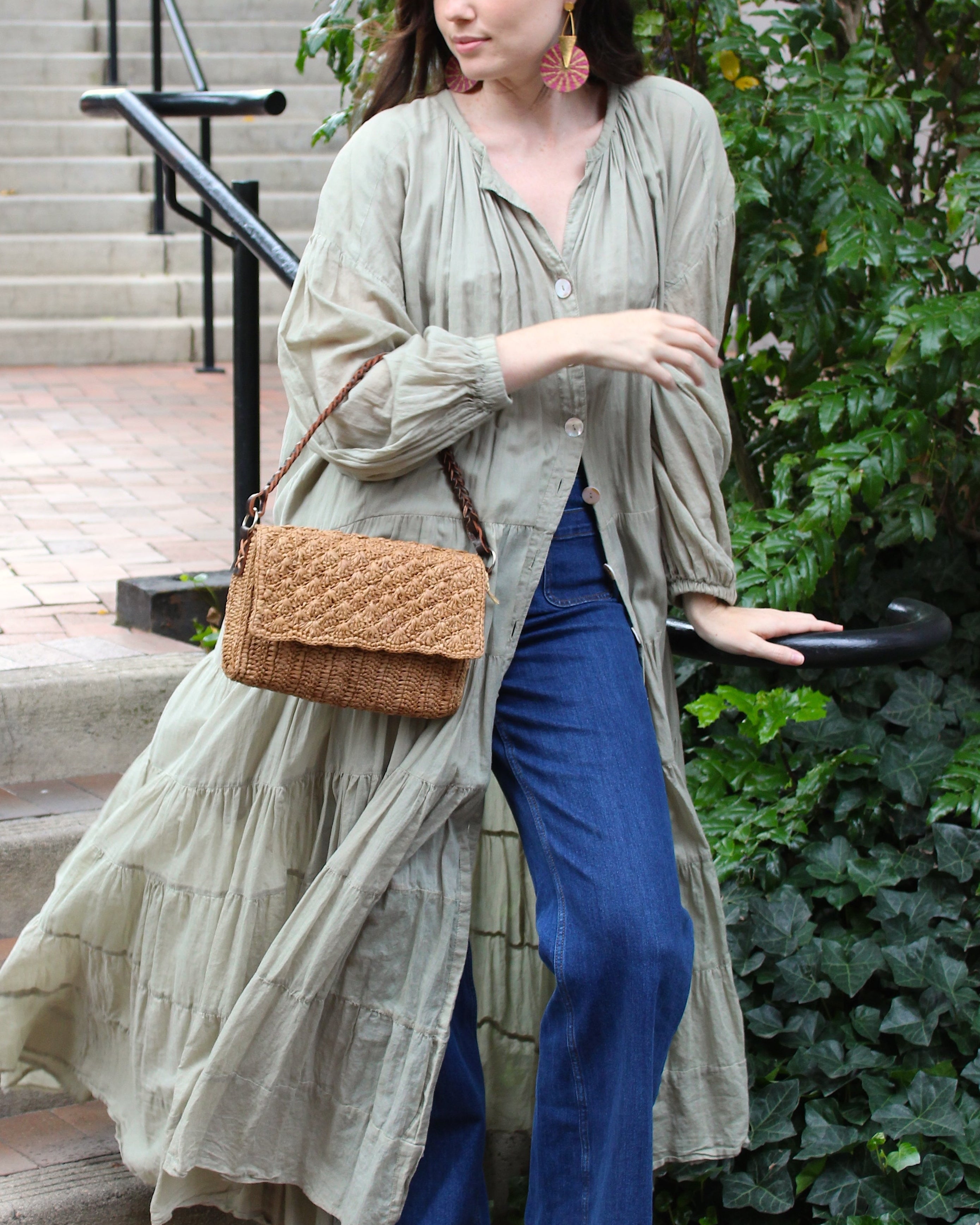 Model wearing Anna Petal Pattern Crochet Straw Over Shoulder Envelope Clutch Purse handmade raffia palm fiber in a solid hue of Cappuccino tea/light/brown crochet in multiple textures resulting in a subtle pattern of vertical linked bands on the bottom half of the bag, and a floral petal or shell pattern on the upper envelope flap with braided leather shoulder strap handbag shoulder bag - Shebobo 