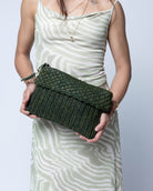 Model wearing Anna Petal Pattern Crochet Straw Pouch Clutch Purse handmade natural raffia palm fiber in a solid hue of Deep Green dark/forrest/green crochet in multiple textures resulting in a subtle pattern of vertical linked bands on the bottom half of the bag, and a floral petal or shell pattern on the upper half - Shebobo