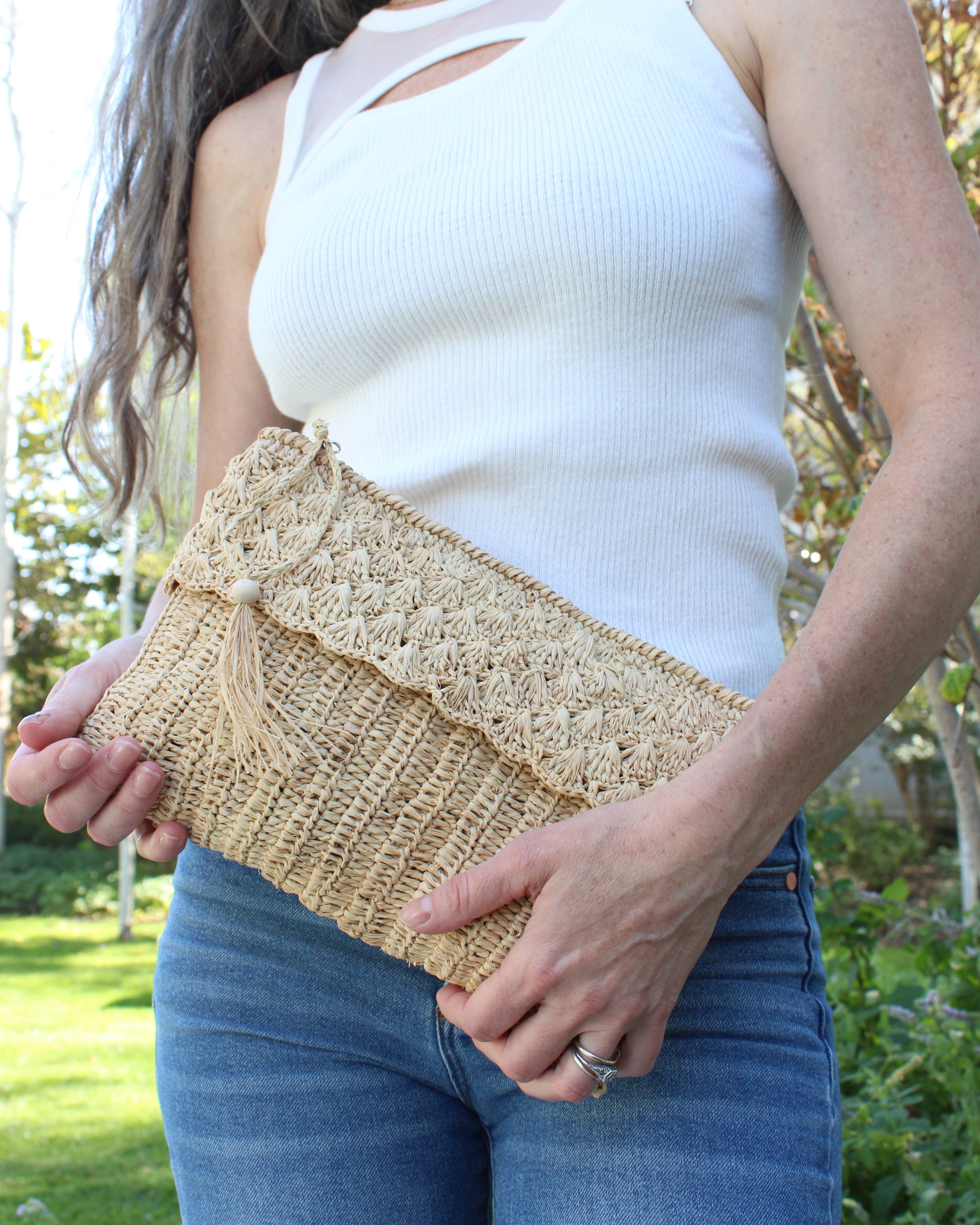 Model wearing Anna Petal Pattern Crochet Straw Pouch Clutch Purse handmade natural raffia palm fiber in a solid hue of Natural straw color crochet in multiple textures resulting in a subtle pattern of vertical linked bands on the bottom half of the bag, and a floral petal or shell pattern on the upper half - Shebobo