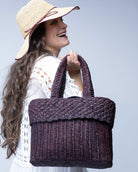 Model wearing Anna Petal Pattern Crochet Straw Basket Handbag handmade natural raffia palm fiber in a solid hue of Espresso chocolate/dark/brown crochet in multiple textures resulting in a subtle pattern of vertical linked bands on the bottom 2/3 of the bag, and a floral petal or shell pattern on the upper third with rolled panel of links making up the handles Beach Bag Purse - Shebobo (with Rachel 4" Brim Crochet Straw Sun Hats with Colored Edge)