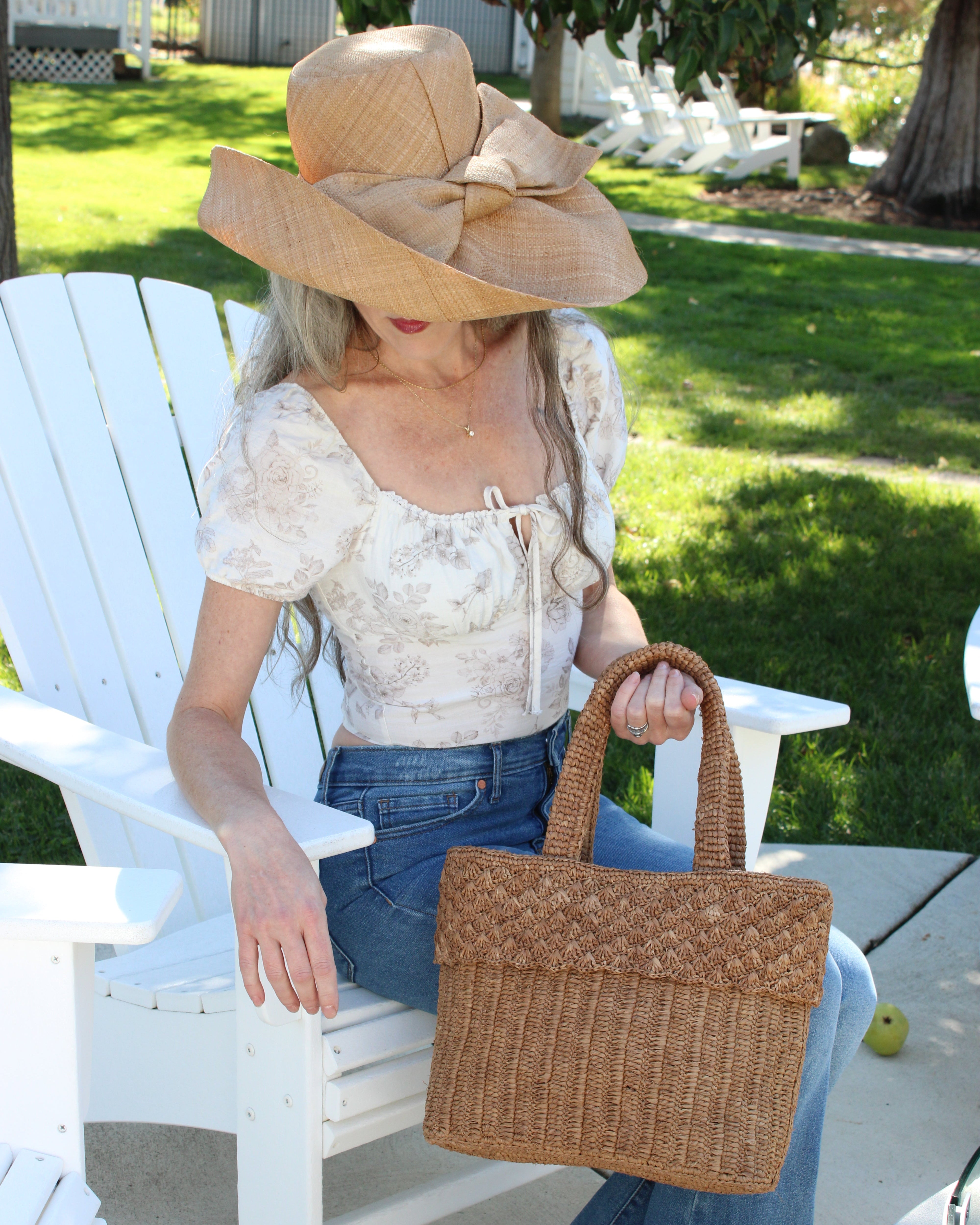 Model wearing Anna Petal Pattern Crochet Straw Basket Handbag handmade natural raffia palm fiber in a solid hue of Cappuccino tea/light/brown crochet in multiple textures resulting in a subtle pattern of vertical linked bands on the bottom 2/3 of the bag, and a floral petal or shell pattern on the upper third with rolled panel of links making up the handles Beach Bag Purse - Shebobo (with Audrey 5" & 7" Wide Brim Big Bow Solid Color Packable Straw Sun Hats)