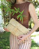 Model wearing Anna Petal Pattern Crochet Straw Pouch Clutch Purse handmade natural raffia palm fiber in a solid hue of Natural straw color crochet in multiple textures resulting in a subtle pattern of vertical linked bands on the bottom half of the bag, and a floral petal or shell pattern on the upper half - Shebobo