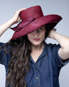 Model wearing Audrey 5" Wide Brim Solid Color Straw Sun Hats with Big Bow handmade loomed natural raffia straw fiber in a solid hue of Umberwine bordeaux/claret/deep/dark/red/purple with matching oversized big bow embellishment hat band - Shebobo