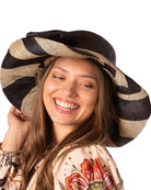 Model wearing Audrey 5" Wide Brim Black Two Tone Wide Stripe Straw Sun Hats with Big Bow handmade loomed raffia palm fiber in a solid hue of Black on the crown and matching oversized big bow embellishment hat band, with two tone even width wide stripe pattern of black and natural straw color that creates a swirl patterned brim - Shebobo