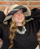 Model wearing Audrey 5" Wide Brim Natural Two Tone Wide Stripe Straw Sun Hats with Big Bow handmade loomed raffia palm fiber in a solid hue of Natural on the crown and matching oversized big bow embellishment hat band, with two tone even width wide stripe pattern of black and natural straw color that creates a swirl patterned brim - Shebobo
