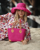Model wearing Augustine Straw Basket Bag handmade loomed raffia handbag with leather corners and handles in fuchsia pink - Shebobo (with Monica 5" Brim Monica Fuchsia Pinstripes Packable Straw Sun Hat) *Tunic by Kikisol