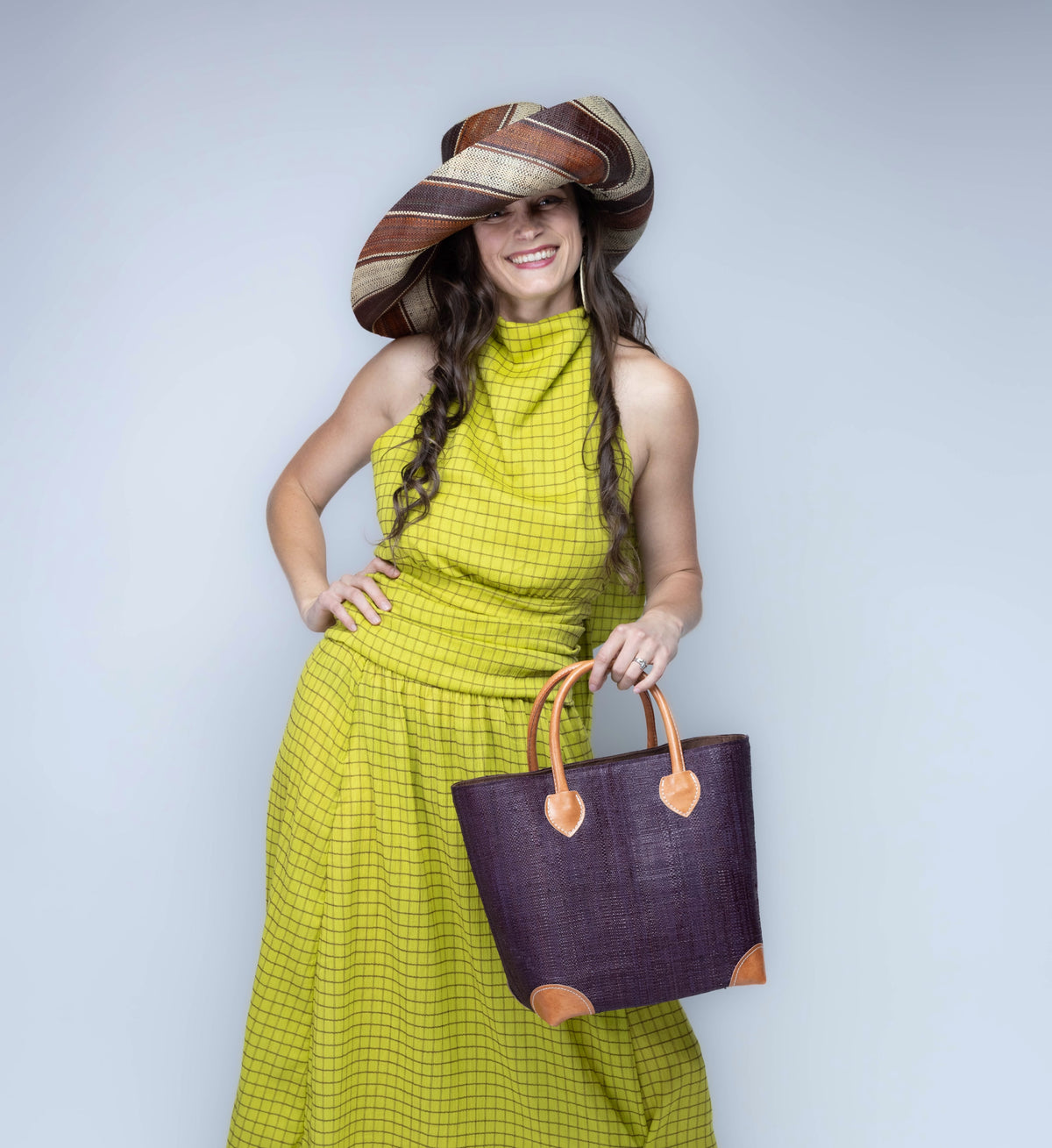 Model wearing Small Augustine Straw Basket Bag Mocha handmade loomed raffia palm fiber in a solid hue of mocha chocolate/dark/brown handbag purse with leather accents and handles beach bag - Shebobo (with Monica 5" & 7" Wide Brim Multicolor Stripe Pattern Packable Raffia Straw Sun Hats)