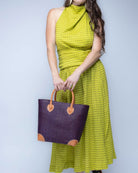 Model wearing Small Augustine Straw Basket Bag Mocha handmade loomed raffia palm fiber in a solid hue of mocha chocolate/dark/brown handbag purse with leather accents and handles beach bag - Shebobo