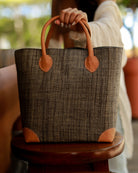 Model wearing Augustine Straw Basket Bag handmade loomed raffia handbag with leather corners and handles in grey - Shebobo