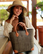 Model wearing Augustine Straw Basket Bag handmade loomed raffia handbag with leather corners and handles in grey - Shebobo (with 4" Brim Rachel Crochet Straw Sun Hats with Colored Edge in Grey)
