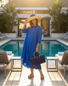 Model wearing Bebe Straw Handbag with Bamboo Handle handmade loomed natural raffia palm fiber in a solid hue of Dusk dark/navy/blue with molded circular bamboo handles, leather feet, and assorted print African wax-cloth fabric liner - Shebobo (with Monica 5" & 7" Wide Brim Two Tone Packable Straw Sun Hats)