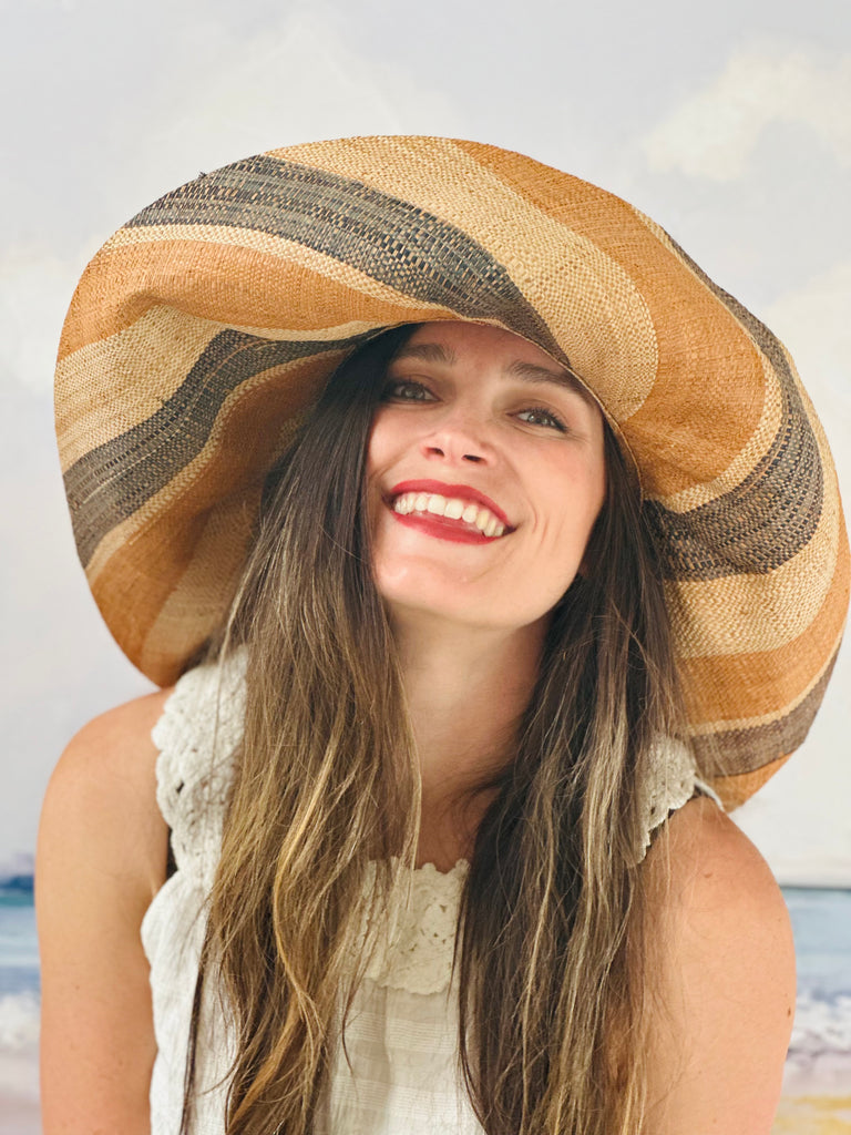 Model wearing 5" & 7" Wide Brim Blush Swirl Multicolor Stripes Packable Straw Sun Hat Handmade loomed raffia in multi width bands of blush orange/pink, grey, and natural create a swirl pattern - Shebobo