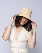 Model wearing Bobbi 3" Brim Crochet Bucket Raffia Straw Hats handmade natural raffia palm fiber in a subtle crochet link texture spiraling out from the top crown of the hat to the edge of the brim in a solid hue of natural straw color with matching braided adjustable hat band sun hat - Shebobo