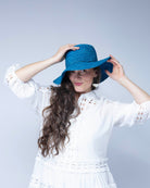 Model wearing 3" Brim Bolero Crochet Straw Sun Hats handmade crochet natural raffia palm fiber in a solid hue of turquoise blue/green making a concentric pattern from the center top of the flattened crown spiraling out to the edge of the brim with matching adjustable raffia braid hat band - Shebobo