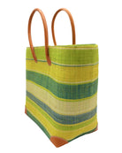Side view Bolinas Izarra Swirl XL Straw Basket Bag handmade loomed natural raffia palm fiber in a multicolor horizontal stripe pattern of multiple width bands of natural straw color, lime green, turquoise blue, navy blue, yellow, etc. with leather handles and accents large tote bag shoulder bag handbag beach bag - Shebobo