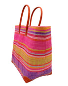 Side view Bolinas Raspberry Swirl XL Straw Basket Bag handmade loomed natural raffia palm fiber in a multicolor horizontal stripe pattern of multiple width bands of natural straw color, red, pink, purple, lime green, yellow, light blue, coral orange, etc. with leather handles and accents large tote bag shoulder bag handbag beach bag - Shebobo
