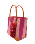Side view Bora Bora Fuchsia Two Tone Stripes Straw Basket Bag with Waterfall Pompoms Charm Embellishment handmade loomed natural raffia palm fiber in a multicolor horizontal stripe pattern of even width wide bands of fuchsia hot/bright/barbie/pink and natural straw color with leather handles and feet plus matching waterfall pompom charm embellishment handbag beach bag - Shebobo