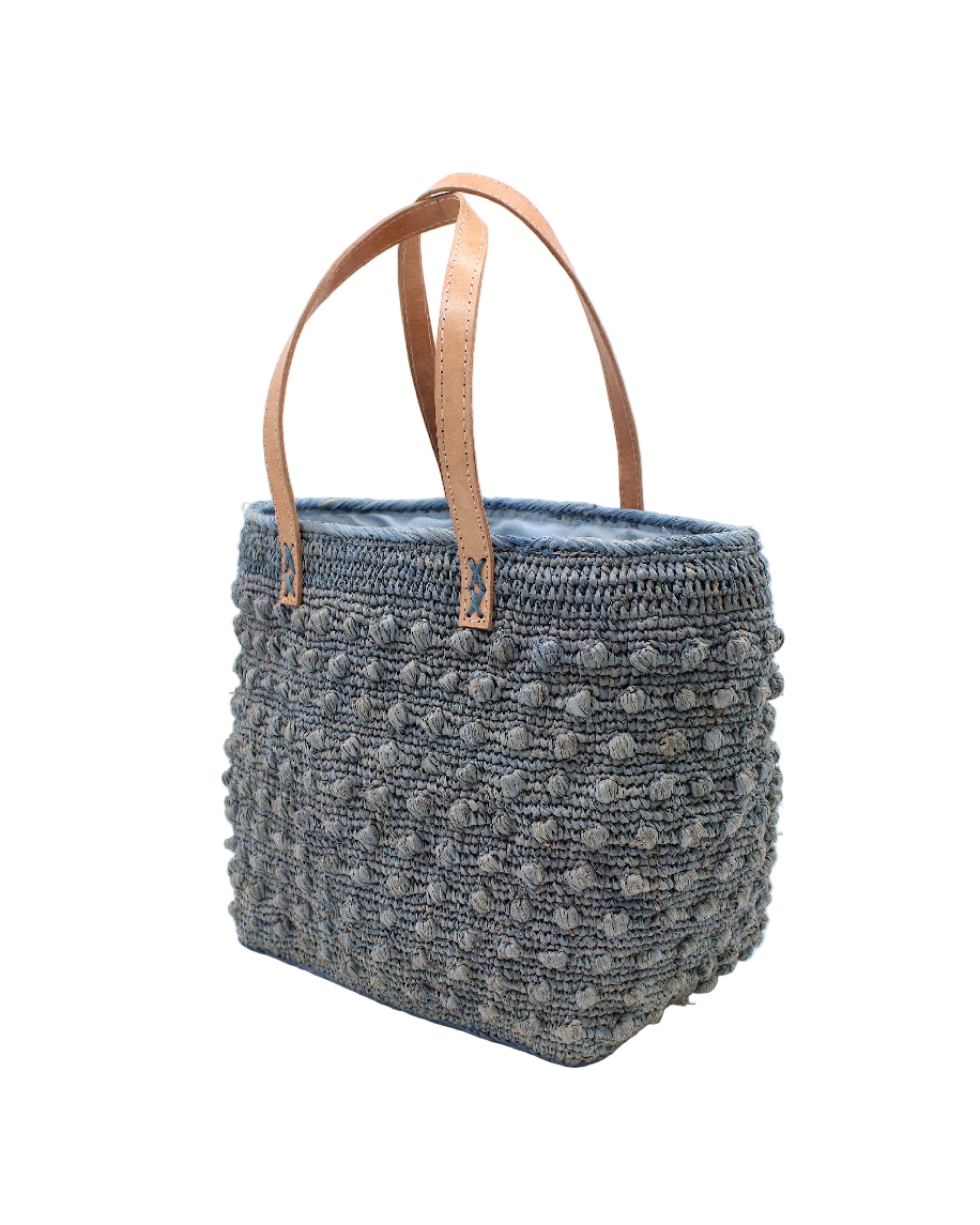 Side view Boucle Denim Crochet Straw Basket Bag handmade woven raffia palm fiber in a solid hue of denim retro/light/blue in a supple nub/ball texture of horizontal bands around the bag with link weave around the top and loop crochet edging on the bottom and top plus leather handles beach bag shoulder bag purse - Shebobo