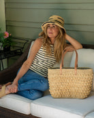 Model wearing Boucle Natural Crochet Straw Basket Bag handmade woven raffia palm fiber in a solid hue of natural straw color in a supple nub/ball texture of horizontal bands around the bag with link weave around the top and loop crochet edging on the bottom and top plus leather handles beach bag shoulder bag purse - Shebobo (with 3" Brim Taylor Crochet Bucket Straw Hats with Zebra Stripe and Lizzie Crochet Straw Sandal)