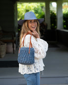 Model wearing Boucle Denim Crochet Small Straw Handbag  handmade woven raffia palm fiber in a solid hue of denim retro/light/blue in a supple nub/ball texture of horizontal bands around the bag with link weave around the top plus assorted print drawstring liner and leather handles  shoulder bag purse - Shebobo (with Panama Unisex Straw Hats)