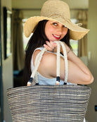 Model wearing 4" Brim Genevieve Natural Crochet Straw Sun Hat with Lace Weave Edge handmade raffia palm fiber crochet solid hue natural straw color rounded crown with detailed lace weave edge and matching adjustable hat band with  Brighton Black Two Tone Multi Melange Straw Beach Tote Bag with Rope Handle - Shebobo