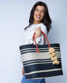 Model wearing Cabrillo Sisal Basket Bag with Waterfall Pompoms Charm Embellishment handmade natural sisal fiber woven into a multicolor two tone Black and natural straw color  horizontal stripe pattern with muti-width bands of color plus leather handles and natural raffia charm shoulder bag beach bag - Shebobo