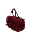 Side view Calypso Pompom Pouf Crochet Straw Basket Handbag handmade natural raffia palm fiber in a solid hue of Umberwine burgunday/bordeaux/dark/purple/red with brushed fringe strands crochet and knotted into a pouf texture with matching wrapped handles purse - Shebobo