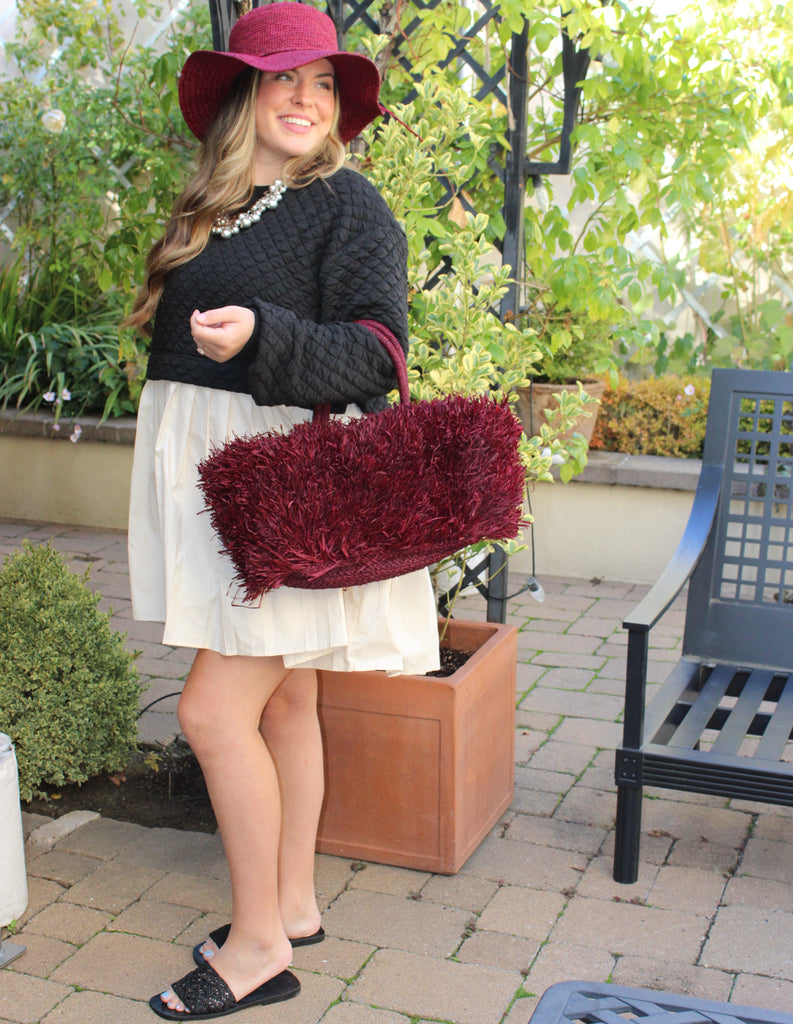 Model wearing Calypso Pompom Pouf Crochet Straw Basket Handbag handmade natural raffia palm fiber in a solid hue of Umberwine burgunday/bordeaux/dark/purple/red with brushed fringe strands crochet and knotted into a pouf texture with matching wrapped handles purse - Shebobo (with Bolero 3" Brim Crochet Straw Sun Hats)