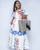 Model wearing Cancun Small Sisal Basket Bag with Tassel Charm handmade natural sisal fibers woven into even width horizontal bands of black and natural straw color that create a pinstripe pattern with matching knotted raffia tufts tassel charm embellishment and leather handles beach bag - Shebobo