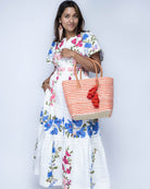 Model wearing Cancun Small Sisal Basket Bag with Tassel Charm handmade natural sisal fibers woven into even width horizontal bands of coral orange and natural straw color that create a pinstripe pattern with matching knotted raffia tufts tassel charm embellishment and leather handles beach bag - Shebobo