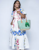 Model wearing Cancun Small Sisal Basket Bag with Tassel Charm handmade natural sisal fibers woven into even width horizontal bands of deep green and natural straw color that create a pinstripe pattern with matching knotted raffia tufts tassel charm embellishment and leather handles beach bag - Shebobo