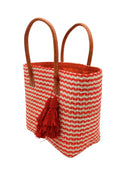 Side view Cancun Small Sisal Basket Bag with Tassel Charm handmade natural sisal fibers woven into even width horizontal bands of coral orange and natural straw color that create a pinstripe pattern with matching knotted raffia tufts tassel charm embellishment and leather handles beach bag - Shebob
