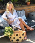 Model wearing Capri Polka Dot Black Small Straw Tote Bag handmade loomed raffia palm fiber in a solid hue of natural straw color with various sized black dots stitched on in a random pattern with leather handles and accents handbag shoulder bag beach bag - Shebobo