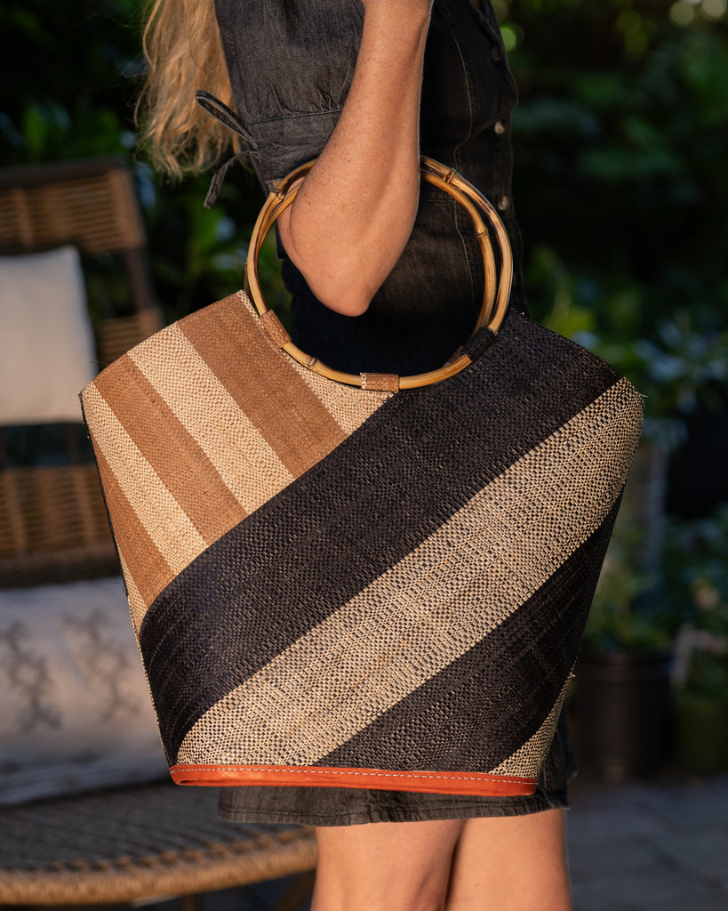 Model wearing Carmen Double Wide Stripe Black & Cappuccino Straw Bucket Bag w/ Bamboo Handle handmade loomed raffia palm fiber in even width wide stripe pattern of black and natural straw color oriented on the diagonal of three quarters of the bag with matching stripe pattern of cappuccino tea/light/brown and natural diagonally on the top left corner quarter shoulder bag handbag - Shebobo