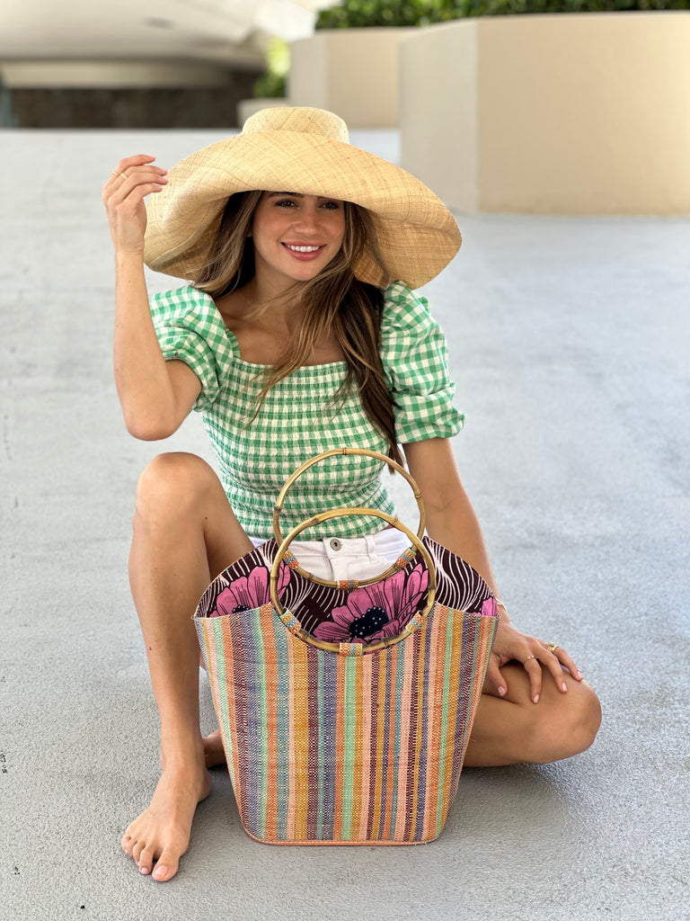 Model wearing Carmen Solid/Stripes Straw Bucket Bag with Bamboo Handles Taffy multicolor vertical stripe pattern of blush, bordeaux, turquoise, orange, saffron, blue, and natural with assorted liner purse - Shebobo (with 7" brim Estrella Natural Straw Sun Hat)