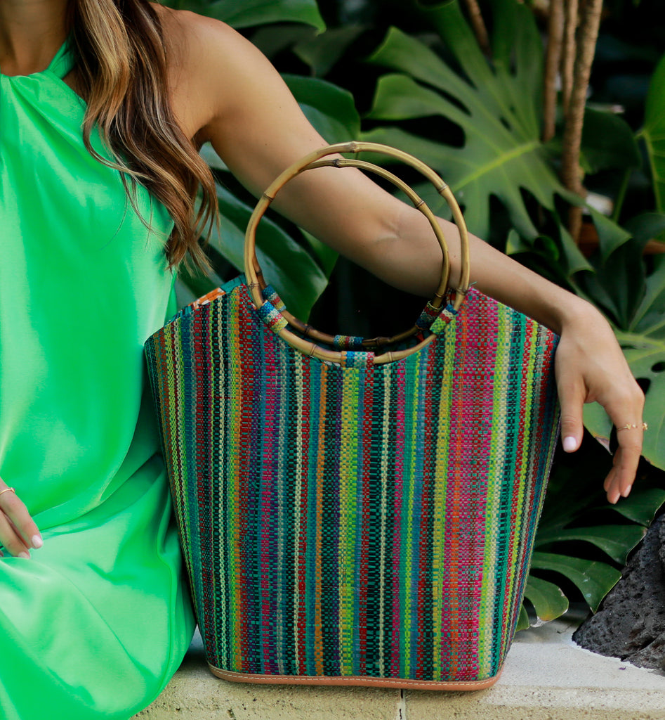Model wearing Carmen Solid/Stripes Straw Bucket Bag with Bamboo Handles Turquoise Stripe multicolor vertical stripe pattern of lime, yellow, turquoise, blue, red, purple, yellow, black, natural, fuchsia, etc with assorted liner purse - Shebobo