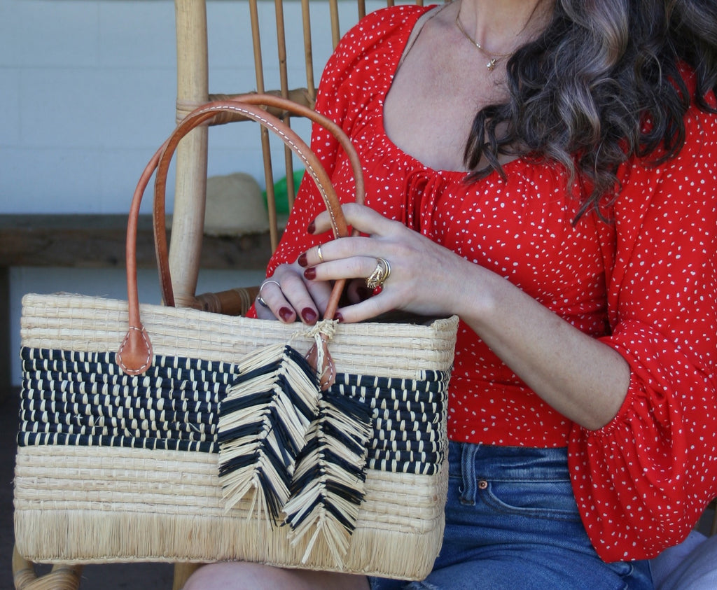 Model wearing Charleston Crochet Rectangle Straw Handbag handmade raffia purse - horizontal stripe pattern of solid natural top, black with natural stitching center, and solid natural base - with two tone black and natural Macrame Feather Charm Embellishment and leather handles - Shebobo