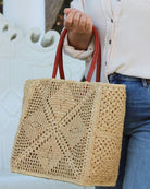 Model wearing Cheval Lace Square Pattern Crochet Straw Basket Bag handmade from natural raffia palm fiber in a lace square geometric diamond pattern with triangle detailing textile in a natural straw color with leather handles handbag purse beach bag tote- Shebobo