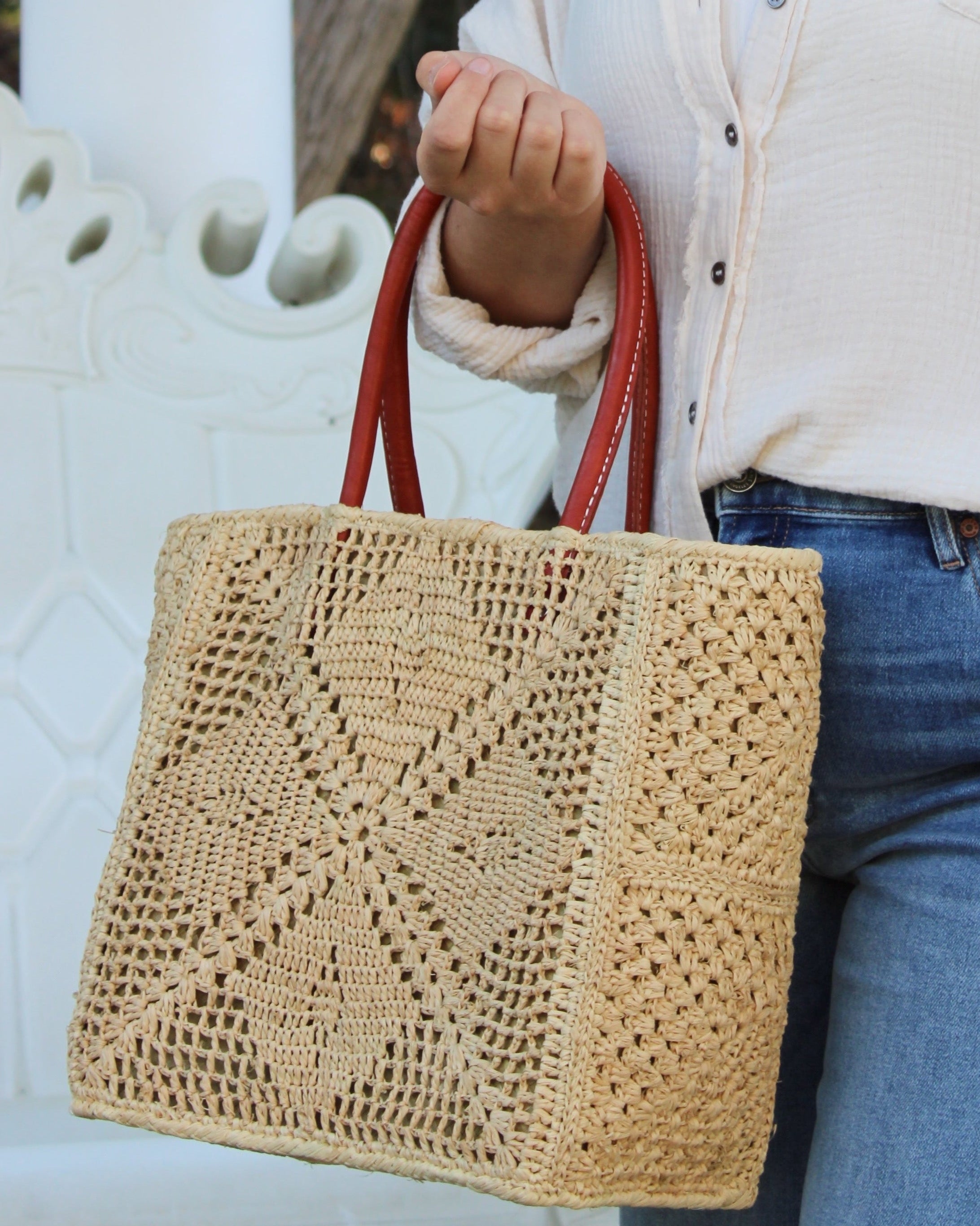 Model wearing Cheval Lace Square Pattern Crochet Straw Basket Bag handmade from natural raffia palm fiber in a lace square geometric diamond pattern with triangle detailing textile in a natural straw color with leather handles handbag purse beach bag tote- Shebobo