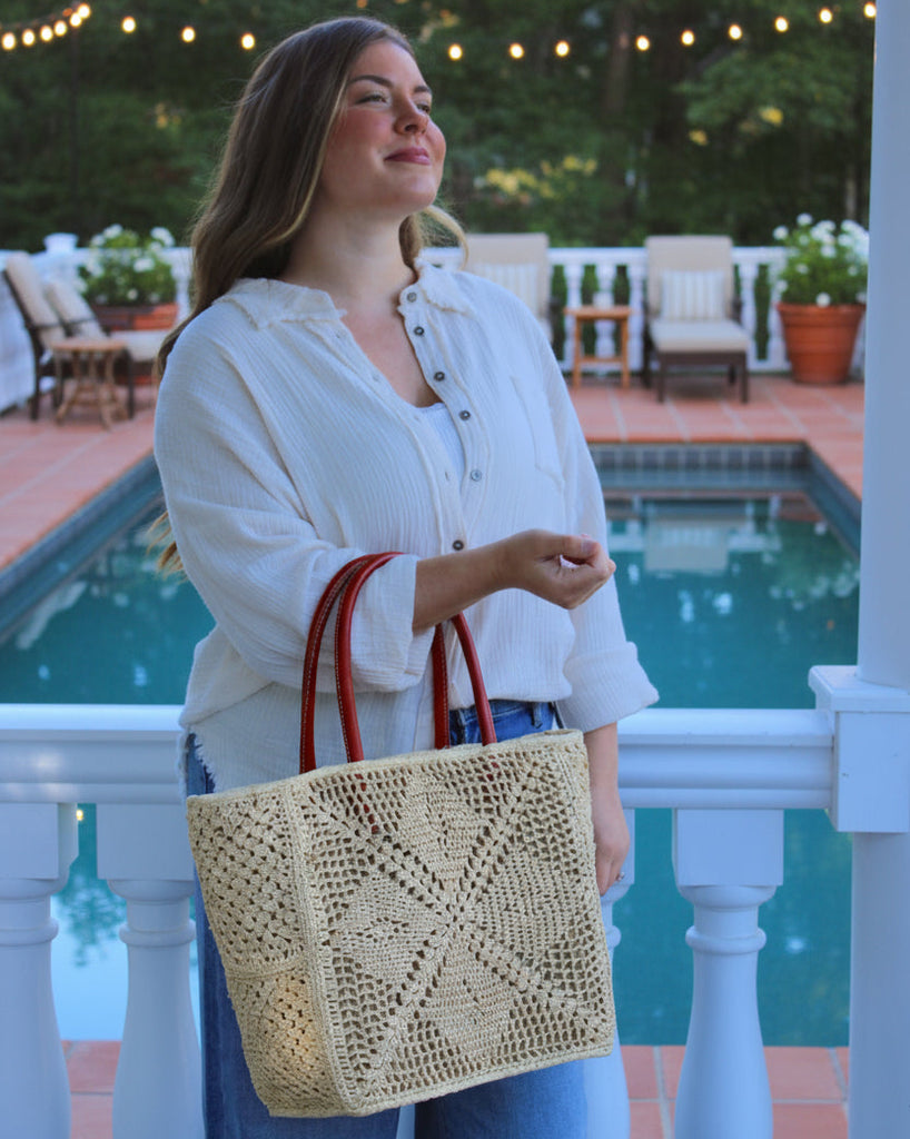 Model wearing Cheval Lace Square Pattern Crochet Straw Basket Bag handmade from natural raffia palm fiber in a lace square geometric diamond pattern with triangle detailing textile in a natural straw color with leather handles handbag purse beach bag tote- Shebobo