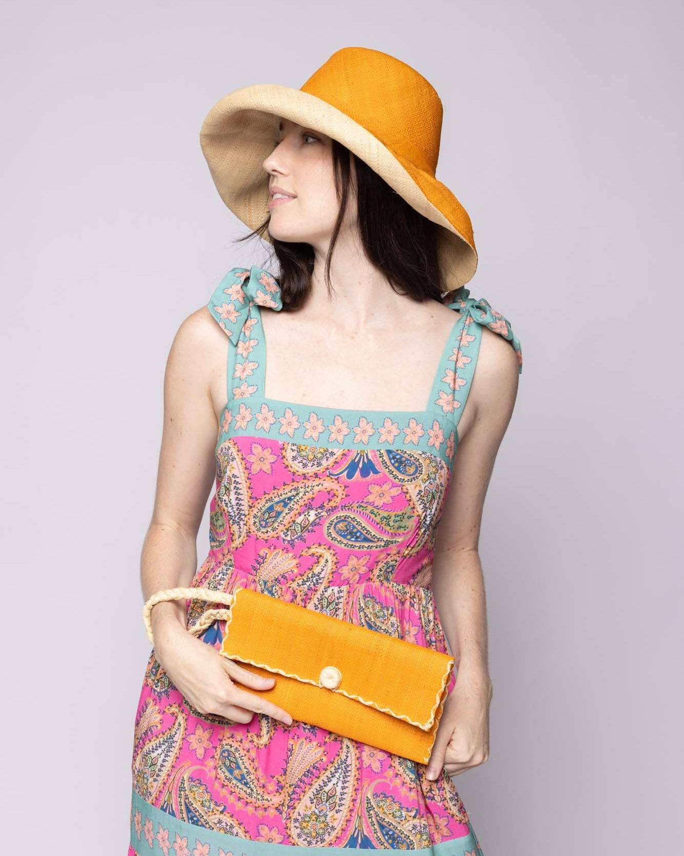 Model wearing ChiChi Saffron Straw Clutch Bag handmade loomed raffia palm fiber wristlet in saffron yellow/orange color with natural straw color cross stitch edging, button & loop closure, and braided wrist strap - Shebobo