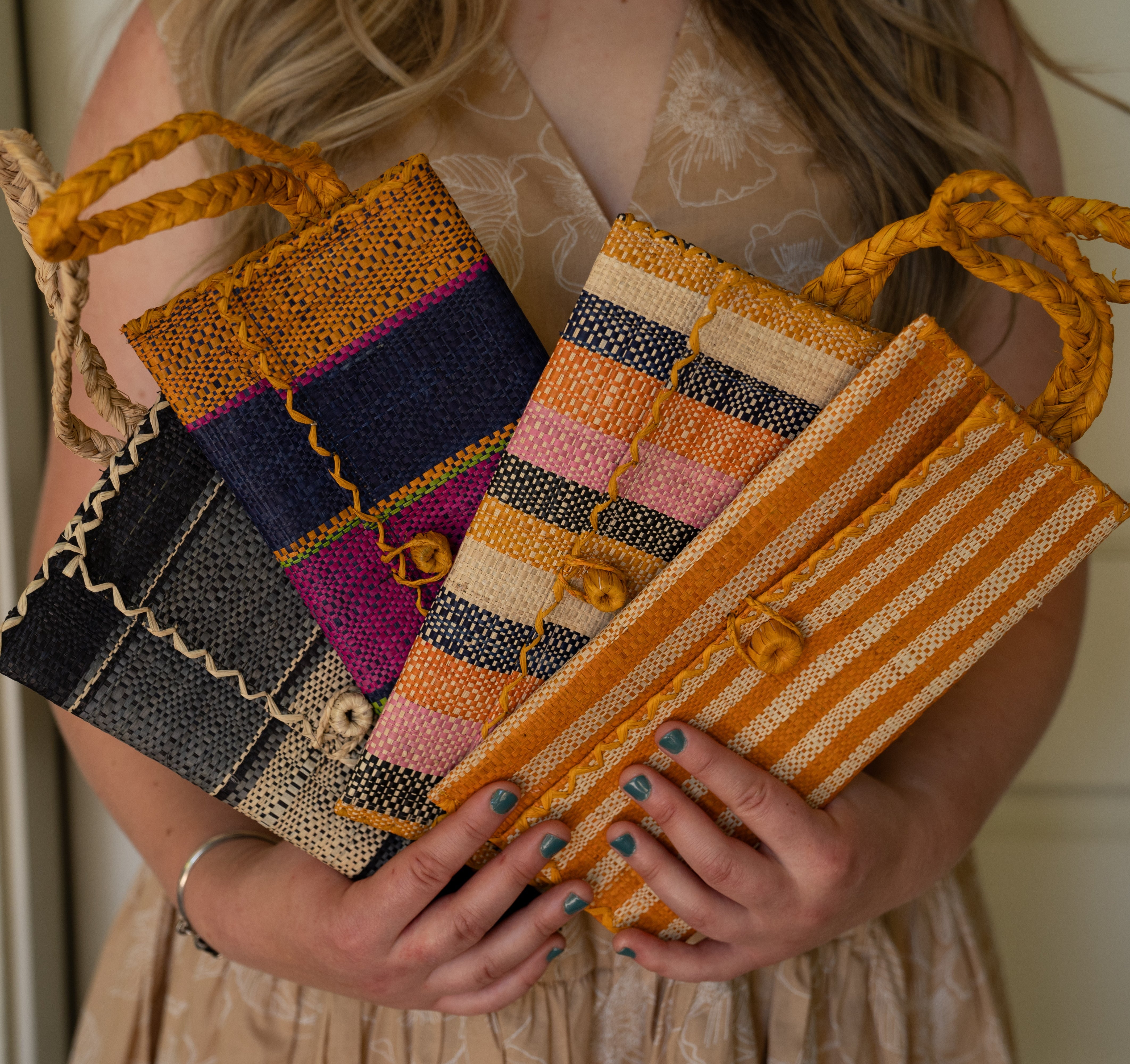 Model wearing multiple solid hues of ChiChi Straw Clutch Wristlet Bag handmade loomed raffia palm fiber in vibrant colors with natural cross stitch edging and raffia loop button closure with matching braided wrist loop with 4" Brim Genevieve Crochet Straw Sun Hats with Lace Weave Edge in Natural Raffia - Shebobo