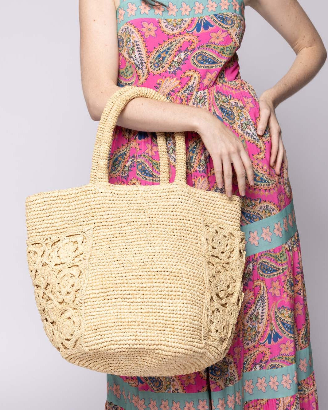Model wearing Colette FlowerCrochet Straw Basket Handbag with Pockets handmade natural raffia palm fiber in a solid hue of natural straw color with geometric granny square floral cutout pattern on two large external pockets tote bag - Shebobo