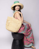 Model wearing Side view Colette FlowerCrochet Straw Basket Handbag with Pockets handmade natural raffia palm fiber in a solid hue of natural straw color with geometric granny square floral cutout pattern on two large external pockets tote bag - Shebobo