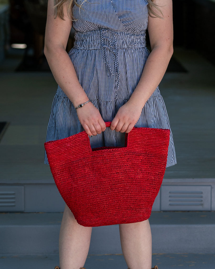 Model wearing ConCon Crochet Straw Basket handmade woven raffia palm fiber in a solid hue of red making a textured link pattern handbag tote - Shebobo