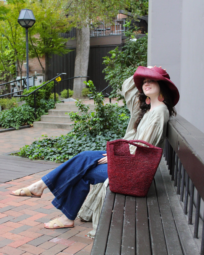 Model wearing ConCon Crochet Straw Basket handmade woven raffia palm fiber in a solid hue of umberwine bordeaux/claret/deep/dark/purple/red making a textured link pattern handbag tote - Shebobo (with Audrey 5" & 7" Wide Brim Big Bow Solid Color Packable Straw Sun Hats and Lizzie Crochet Straw & Leather Sandal Shoes)