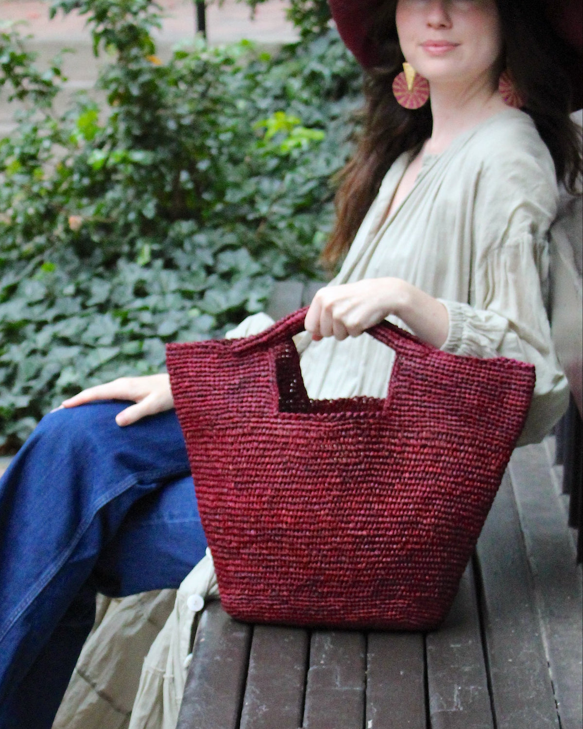 Model wearing ConCon Crochet Straw Basket handmade woven raffia palm fiber in a solid hue of umberwine bordeaux/claret/deep/dark/purple/red making a textured link pattern handbag tote - Shebobo