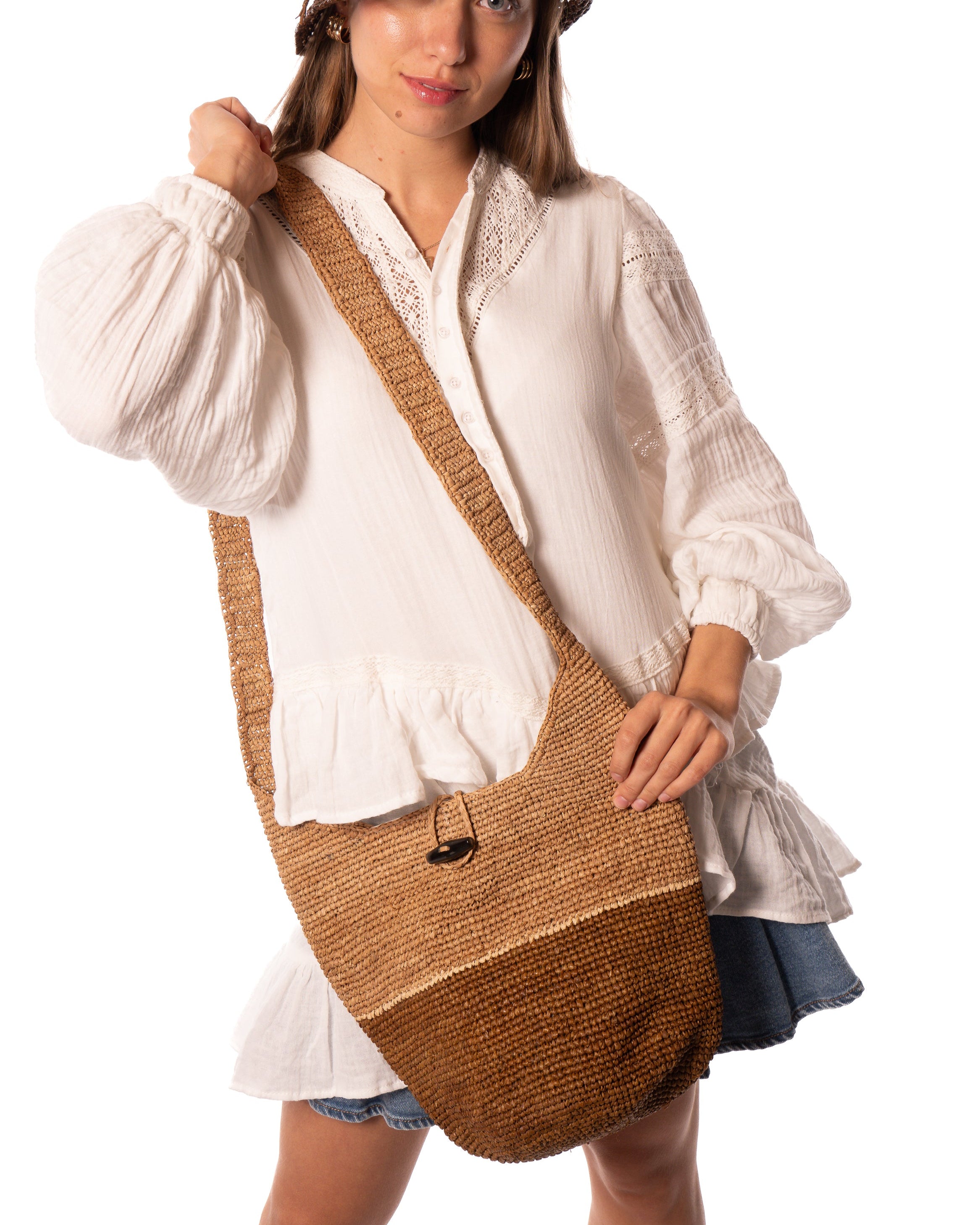 Model wearing Coronado Two Tone Crochet Crossbody Bag handmade with interior liner, horn button and loop closure raffia purse cinnamon/tobacco/dark brown bottom, with narrow natural straw color horizontal stripe separating light brown/tea colored top & shoulder strap - Shebobo (with 2.5" Brim Maria Crochet Cloche Bucket Straw Hats Cinnamon/Tobacco/Brown) 