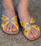 Model wearing Daisy Crochet Straw & Leather Sandal with Flower Embroidery & Metallic Detailing handmade crochet natural raffia palm fiber in a solid hue of natural straw color in two bands with saffron yellow petals and coral orange/red centered embroidered flower pattern wrap around the top  of the shoe with a band of metallic gold across the top summer sandals shoes - Shebobo
